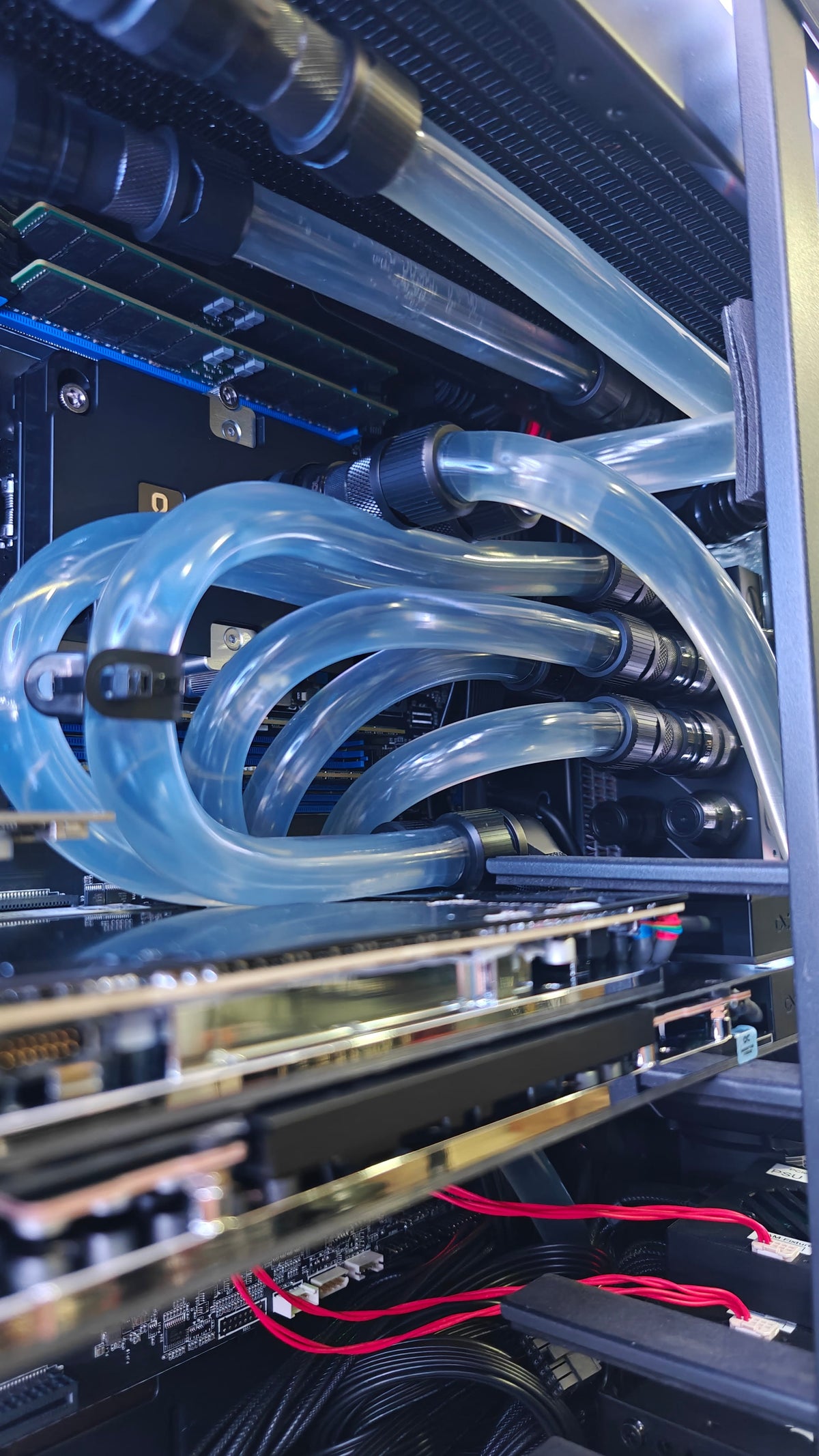 Close-up of a custom liquid CPU cooler with clear transparent tubes and black fittings installed inside a computer case.